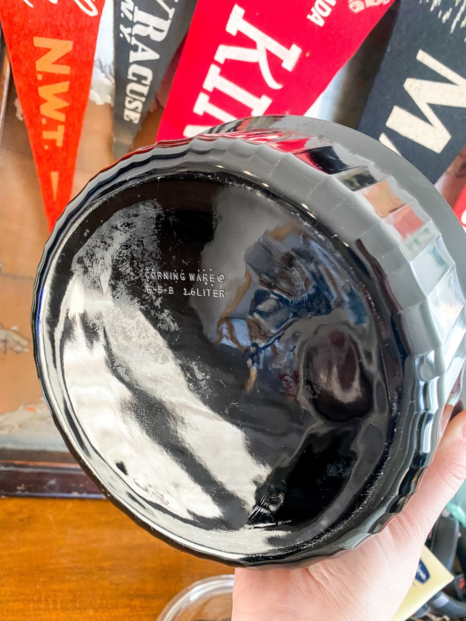 A woman holds the dish in focus so that the back of the dish is visible. It reads, "Corningware565 1.6Liter" 