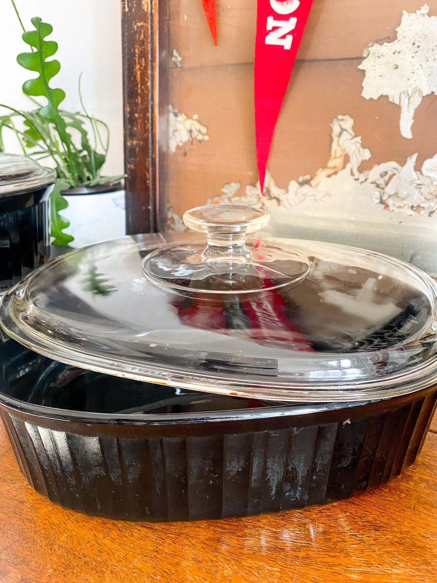 The black casserole dish is in full focus with the dish sitting on a wooden top. The clear, round lid is partially off to show the inside. The exterior black base is fluted to the top where it meets the lid.  