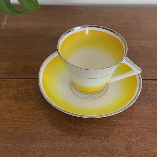 Video of Gladstone teacup with triangle/angular handle. Colour is a bright yellow that fades into the white. Rims of silver or white gold appear on cup. 