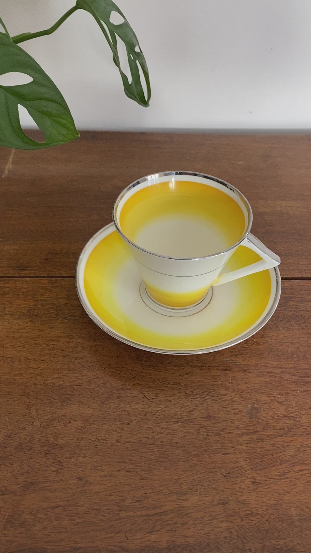 Video of Gladstone teacup with triangle/angular handle. Colour is a bright yellow that fades into the white. Rims of silver or white gold appear on cup. 
