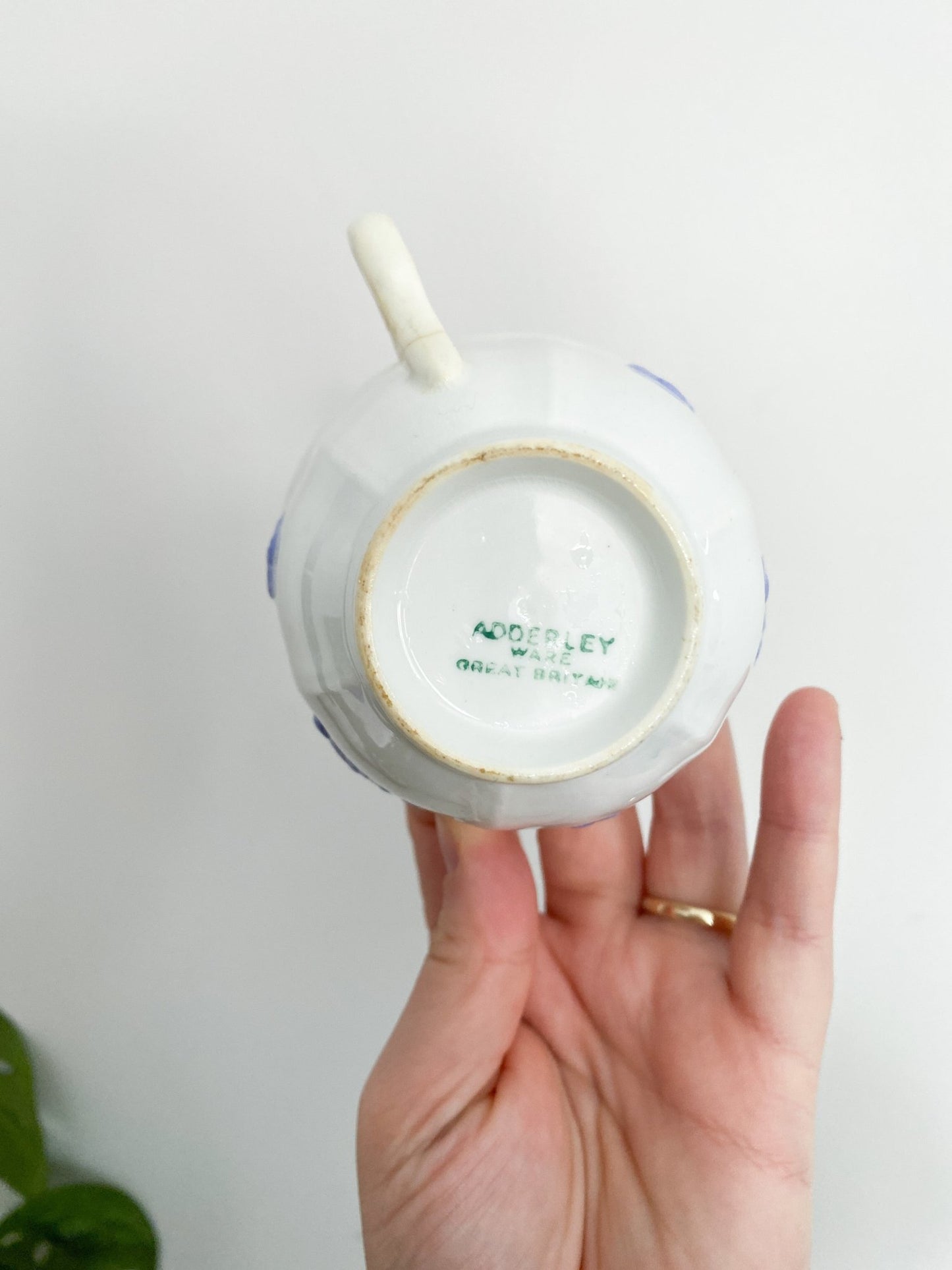 Woman holding Adderley tea cup in her hand. The woman is showing the cup&#39;s backside where the stamp resides. The teacup is white and the stamp is worn with the green logo that says "Adderley Ware Great Britain"