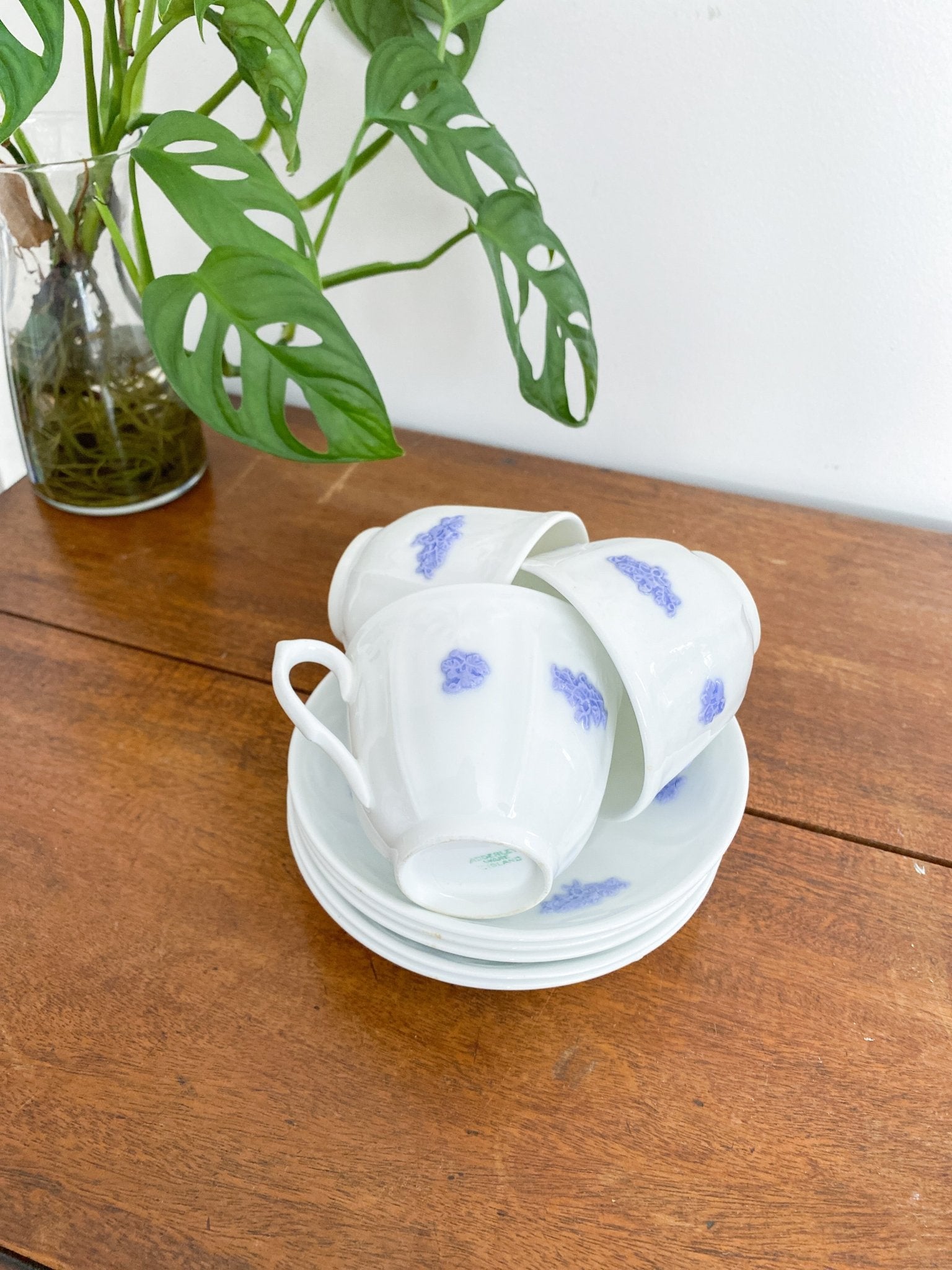 There are three teacups stacked on the saucers within eachother on a wooden table. The teacups are all upright but the handle is facing separate directions. The teacups are on the saucers and show the blue or violet colours.