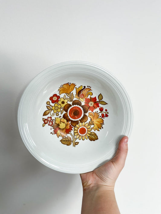 A woman is holding the bowl facing the camera with the inside of the bowl showing. The inner bowl has a scene of many flowers in different variations and colours ranging in red, yellow and orange.