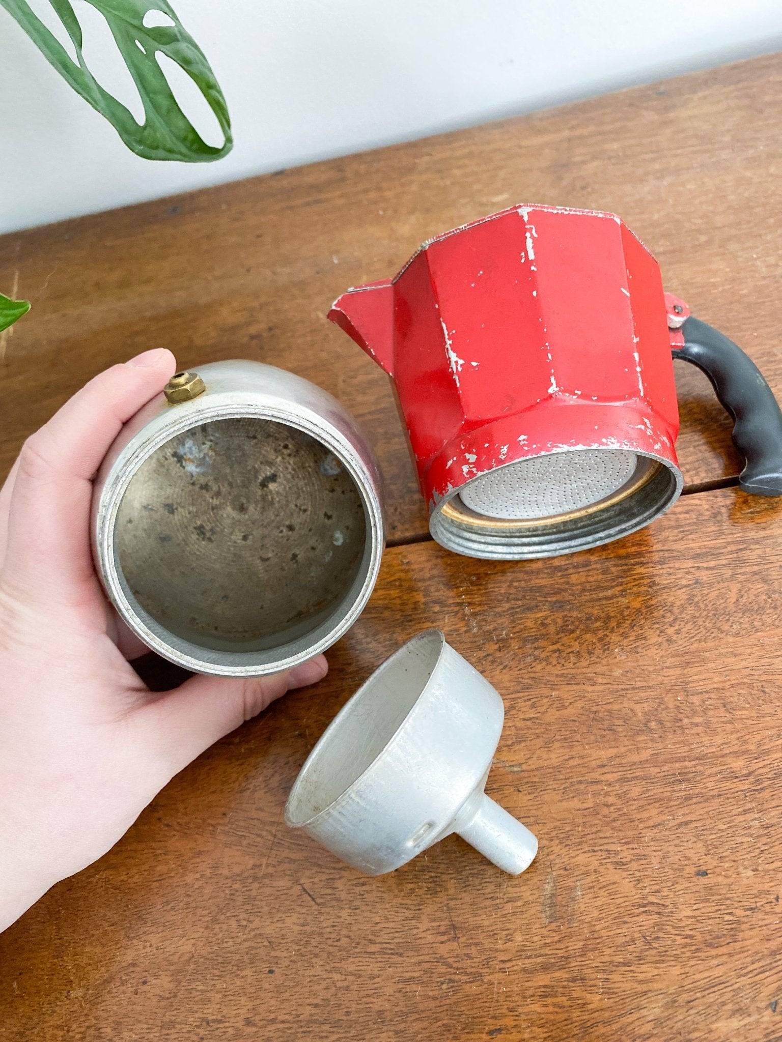 A closeup of the moka pot to show the separate pieces. The base with some age shown inside, the espresso cup and the red top. 