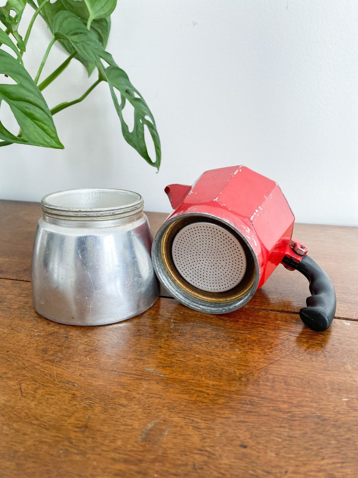 A closeup of the moka pot to show the separate pieces. The base with some age shown inside and the red top.