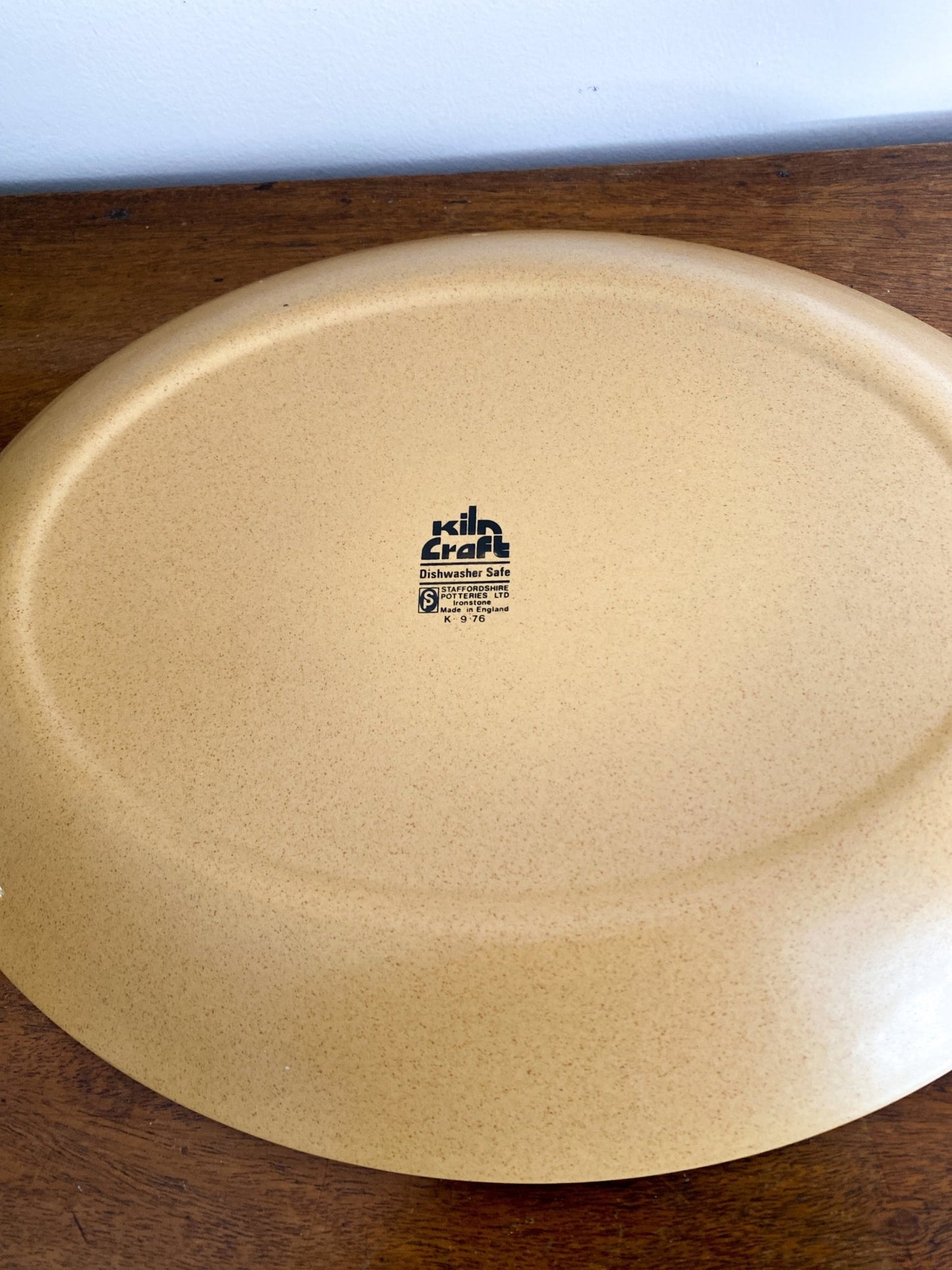 The serving tray is upside down on the wooden table to show the makers stamp. It is a faraway picture of the tray. 