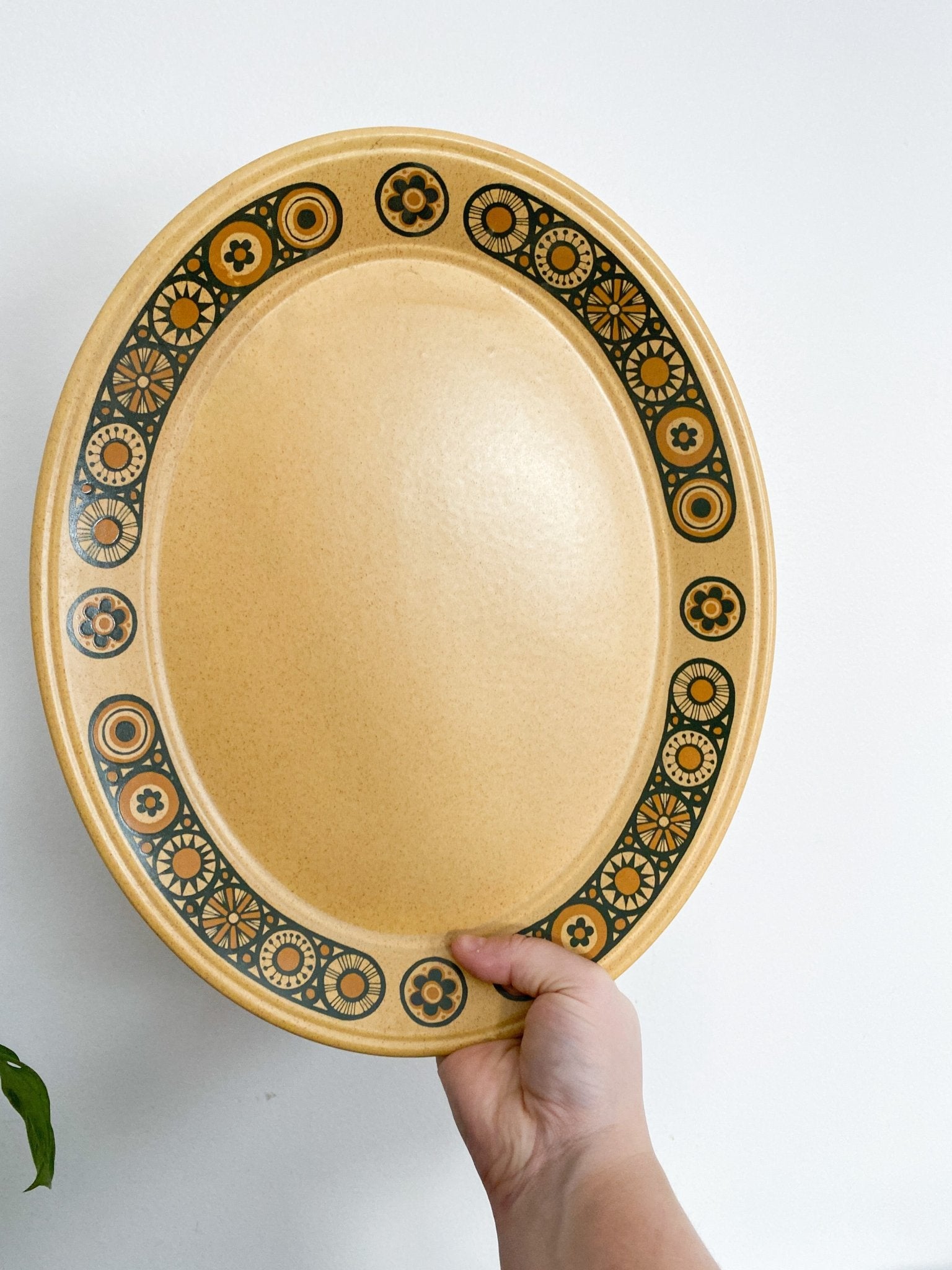 A woman holds the tray upright in her hand. The tray is a brownish-honey colour with flowers along the rim that are outlined in black and fulled in colours of burnt orange. There is a leaf in the bottom left.