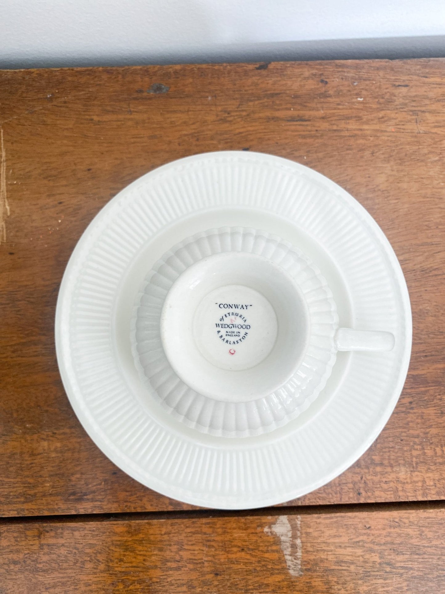 A teacup sits on upside down on top of a lunch plate, it shows the exterior of the cup with the Wedgwood stamp on the bottom. The creamy colored lunch plate has a dotted edge. 